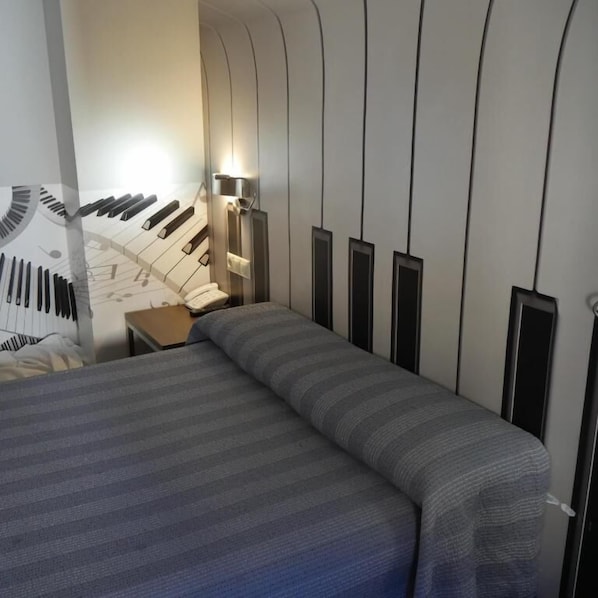 A hotel room with a bed, a nightstand, a lamp, and a wall with vertical lines.
