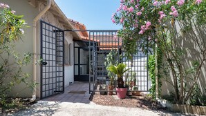 Un patio amurallado con plantas en macetas y una palmera, que da acceso a un edificio con techo de tejas.