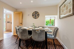 A dining area with a wooden door, a wall clock, and a window with a view of greenery. - Spacious 3BR House in Blackburn, Garden, Free WiFi & 4-Car Parking (Blackburn)