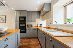 A modern kitchen with grey cabinets, a wooden countertop, a built-in oven, and a window with a view. - Spacious 3BR House in Blackburn, Garden, Free WiFi & 4-Car Parking (Blackburn)