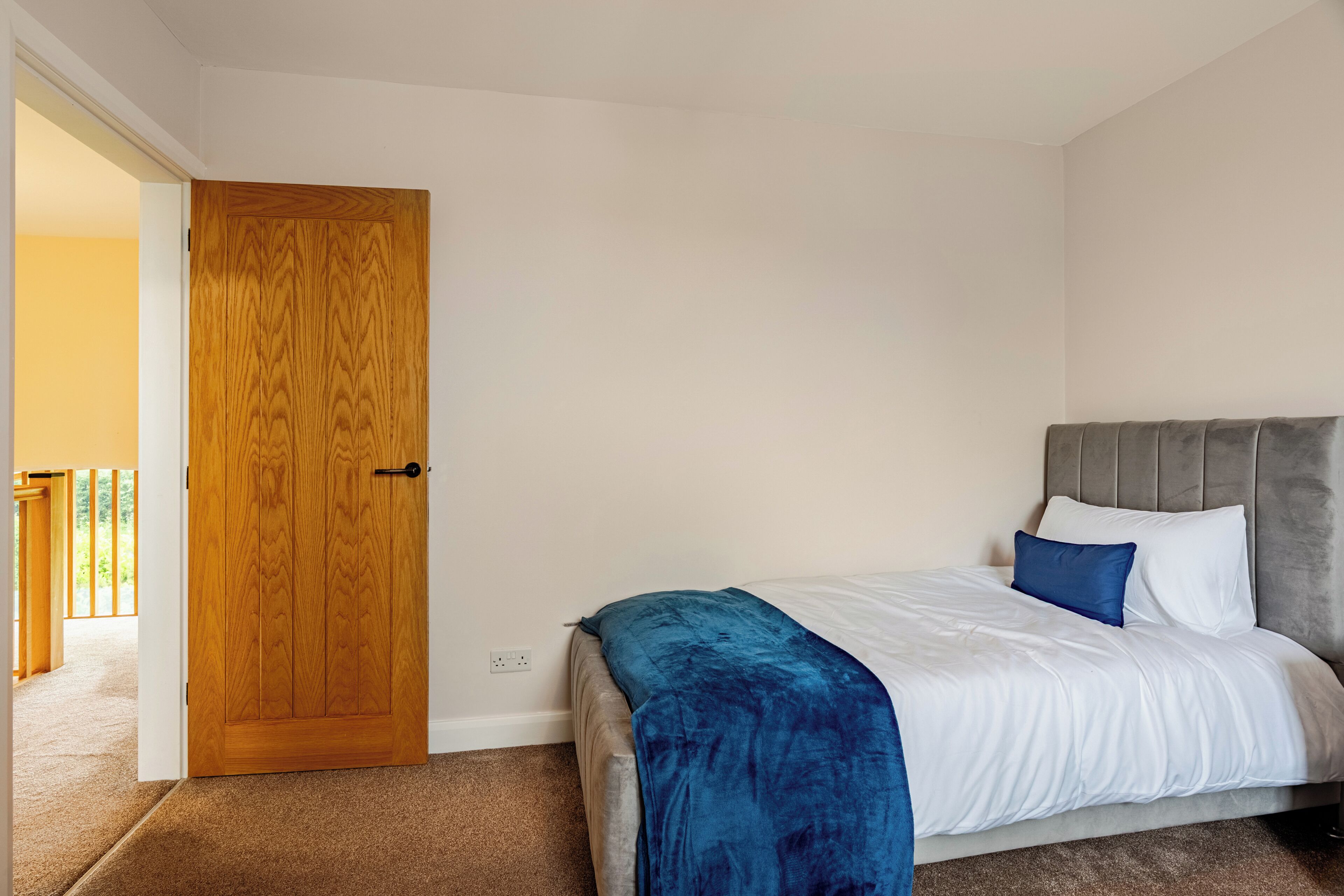 A bedroom with a bed, a wooden door, and a view of a balcony.