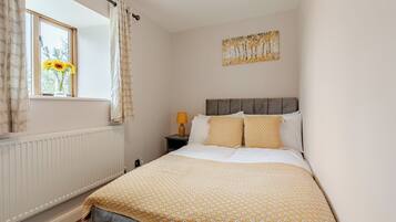 A bedroom with a bed, a window with curtains, a bedside table with a lamp, and a wall-mounted painting.