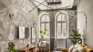 A modern living room with a wooden coffee table, a sofa, a TV mounted on the wall, and a large window with arched tops. - Kleparz modern by Fragola Apartments (Kraków)