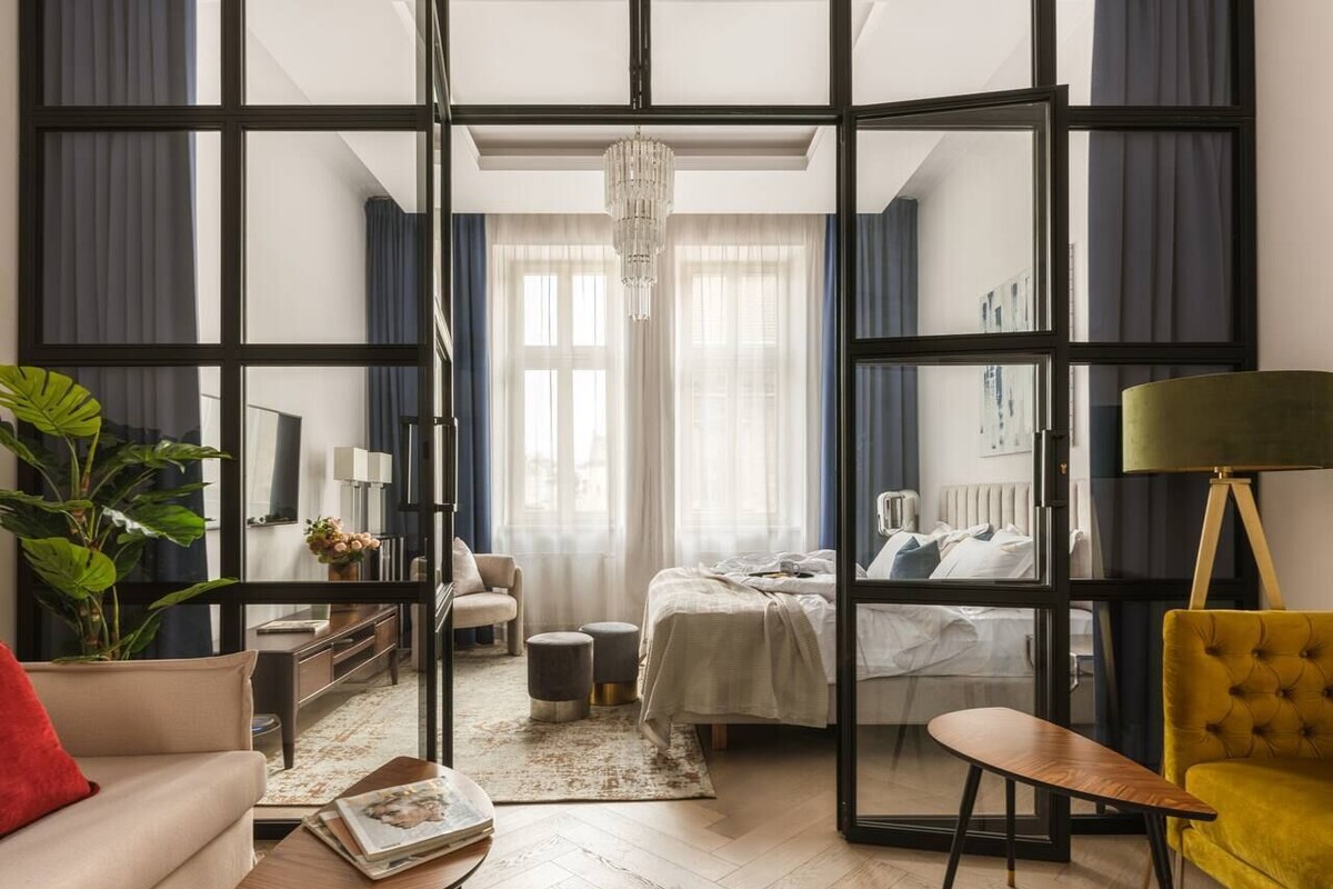A modern hotel room with a large sliding glass door, a bed, a sofa, a coffee table, and a floor lamp.