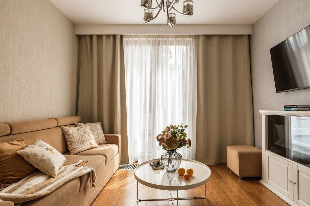 A modern living room with a sofa, a coffee table with flowers, a television, and a cabinet.