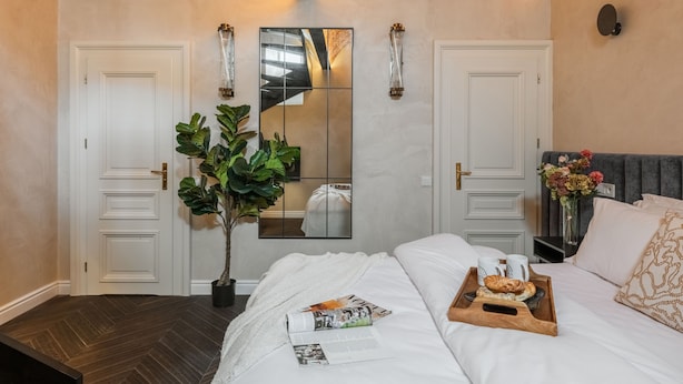 A bedroom with a large bed, a mirror, two doors, a potted plant, and a tray with breakfast items. - Kleparz modern by Fragola Apartments (Kraków)