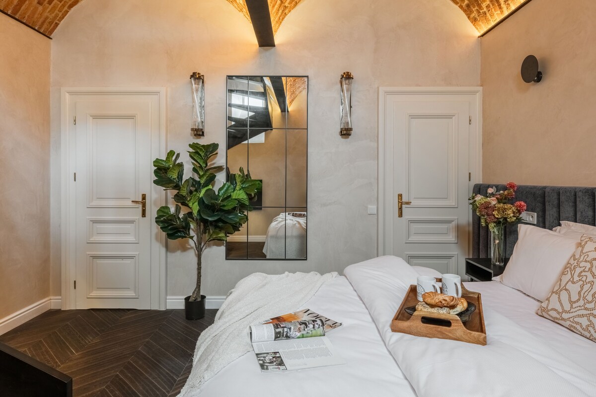 A bedroom with a large bed, a mirror, two doors, a potted plant, and a tray with breakfast items.