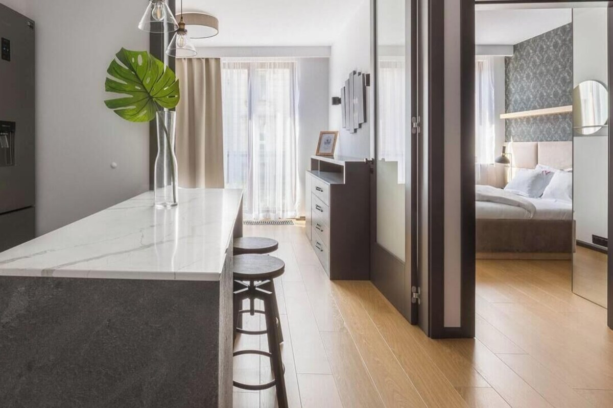 A modern kitchen with a marble island, bar stools, and a large plant.