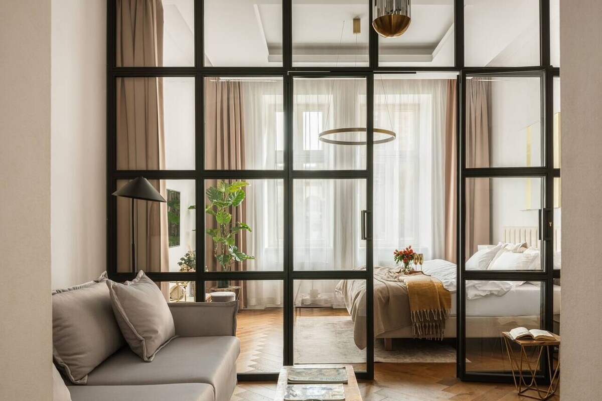 A modern living room with a sofa, coffee table, and a bed with a view through a large window.