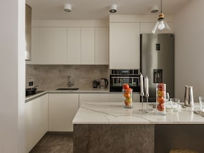 Uma cozinha moderna com armários brancos, bancada de mármore, geladeira de aço inoxidável e luminária pendente.