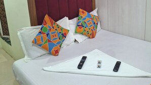 A hotel room with a bed, two colorful pillows, two remote controls, and a ceiling fan. - Venus Guest House  (Mumbai)