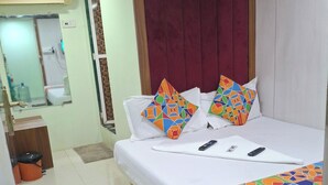 A hotel room with a bed, pillows, a remote control, and a patterned bedspread. - Venus Guest House  (Mumbai)
