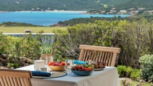 Una mesa con vista a un paisaje costero, un cuenco de fruta y un jarrón con lavanda.