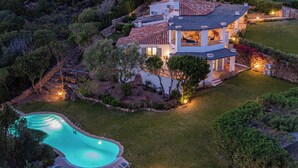 Una casa grande con piscina, rodeada de exuberante follaje y un césped cuidado.