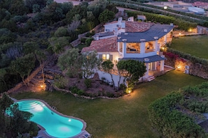 Una casa espaiosa amb piscina, envoltada de vegetació exuberant i un jardí ben cuidat.