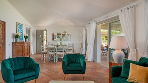 Una sala de estar con dos sofás verdes, una mesa de centro blanca y un comedor con una mesa y sillas.