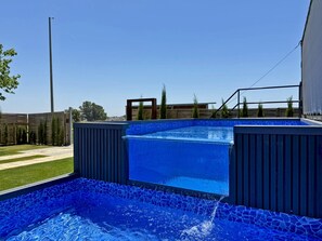 Ein Schwimmbecken mit blauem Mosaikfliesenmuster, umgeben von einer Holzterrasse und einem Zaun.