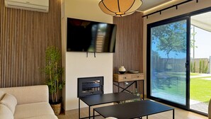 A modern living room with a sofa, a coffee table, a TV, and a sliding glass door leading to a backyard. - Casa Las Mironas - III - Ole Solutions (Puerto de Santa María)