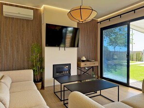 Ein modernes Wohnzimmer mit Sofa, Couchtisch, Fernseher und einer Schiebetür zu einem Garten.