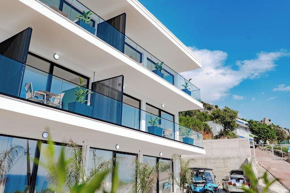 A modern multi-story building with balconies, large windows, and potted plants.