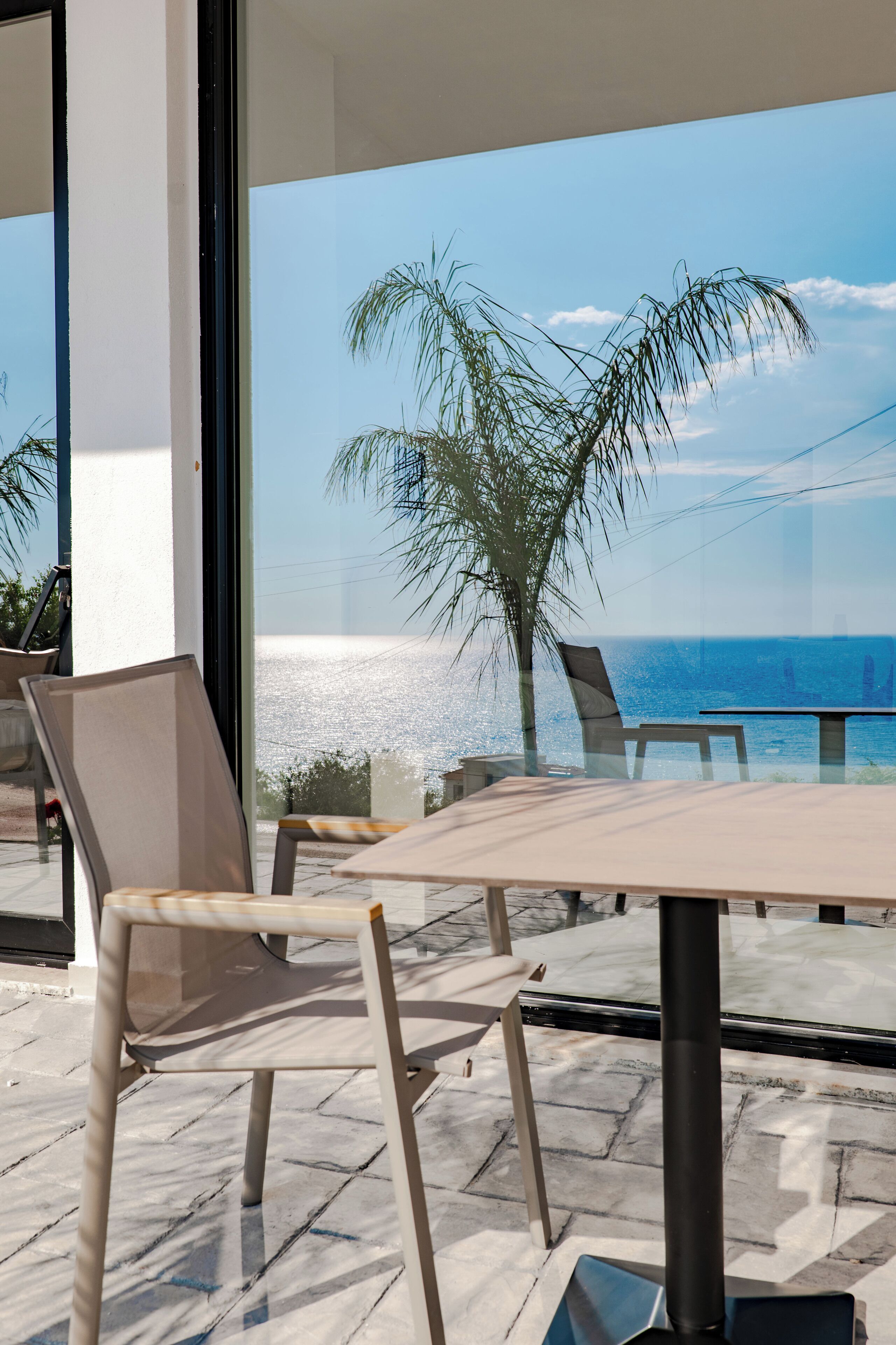 Un espace extérieur moderne, aménagé avec une table et des chaises, offrant une vue sur une plage et des palmiers.