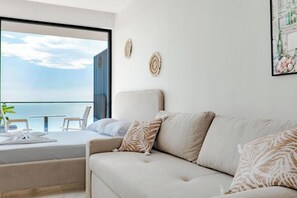 A modern hotel room with a large window, a balcony, a sofa, and decorative wall art. - SeaScape Residence (Borsh)