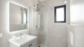 Un bagno moderno con doccia vetrata, uno specchio grande e una finestra.