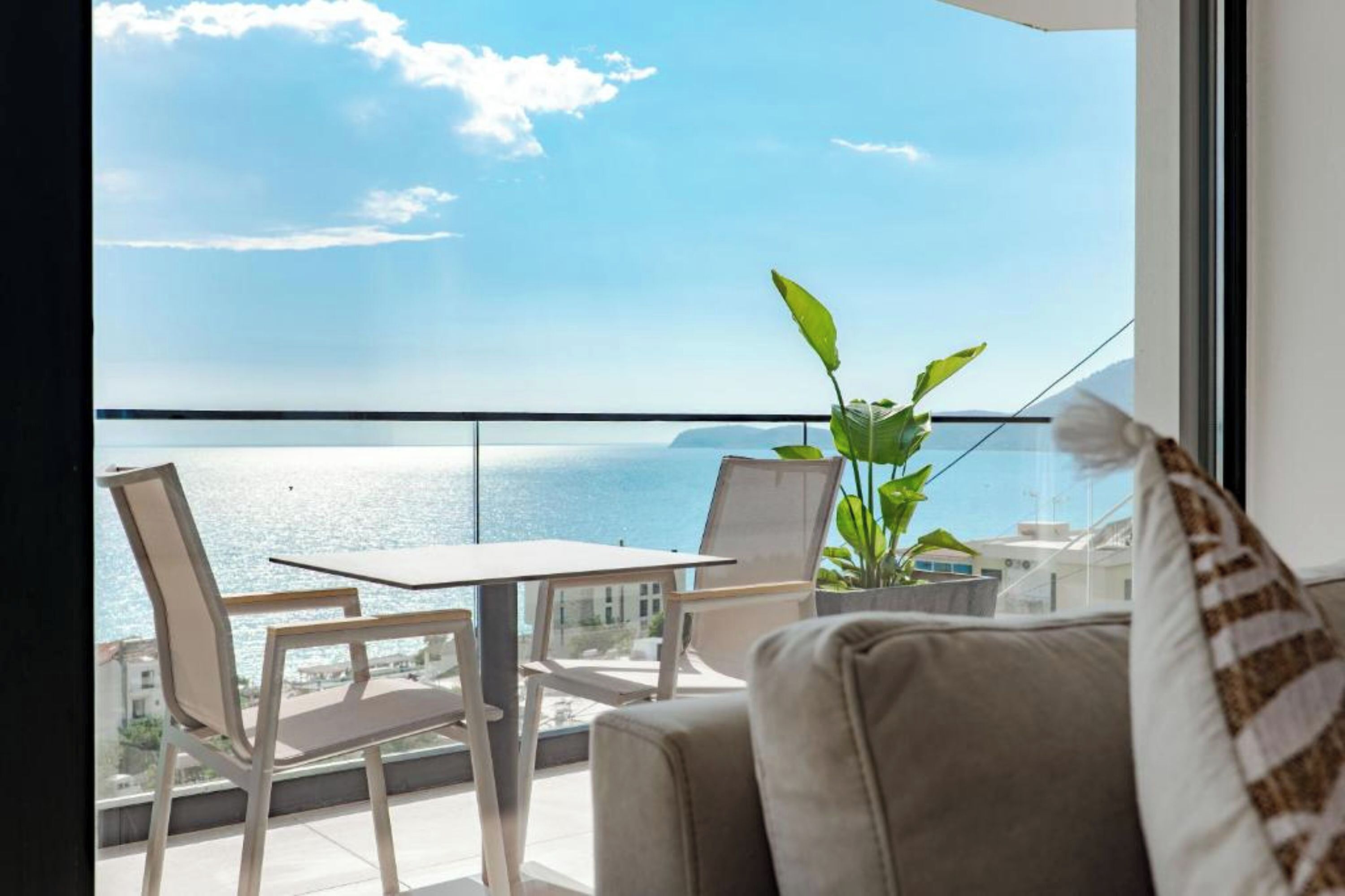 Un balcón con vista al mar, una mesa, sillas y una planta en maceta.