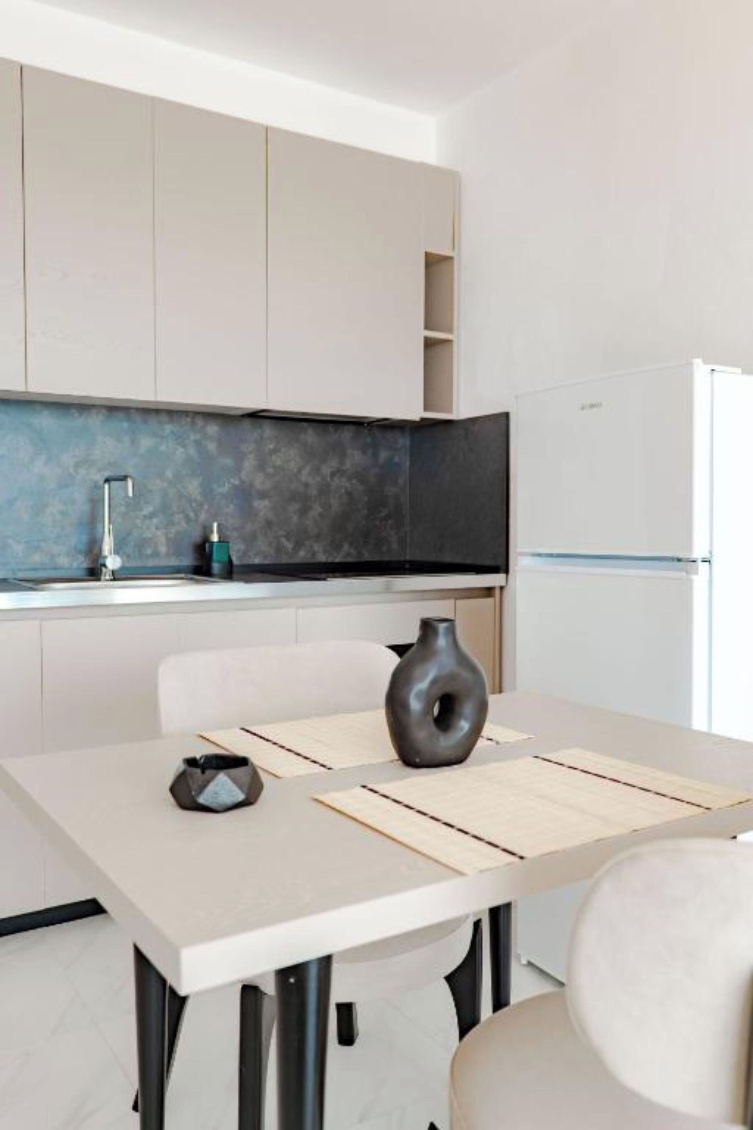 Una cocina moderna con una mesa de comedor, sillas, un jarrón y un refrigerador.