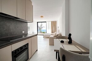 A modern kitchen with a stove, oven, and a dining area with a table and chairs. - SeaScape Residence (Borsh)