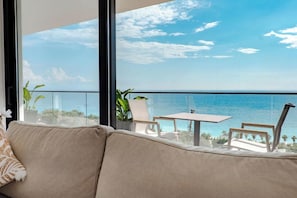 A balcony with a view of the sea, a sofa, and a table with chairs.