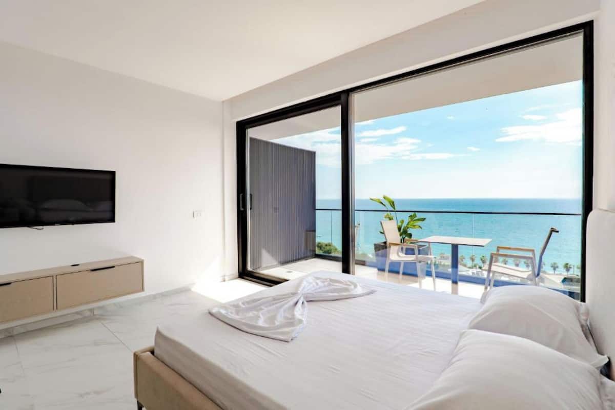Un dormitorio con una cama grande, un televisor montado en la pared y un balcón con vista al mar.
