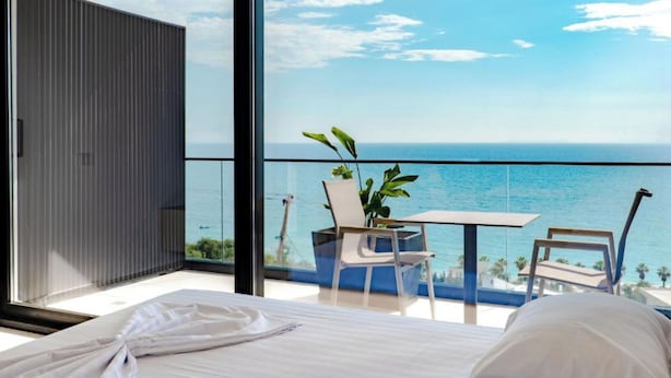 A bedroom with a large window, a bed, and a view of the ocean. - SeaScape Residence (Borsh)
