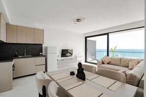 A modern living space with a kitchen, dining area, and a large window with a view of the sea. - SeaScape Residence (Borsh)