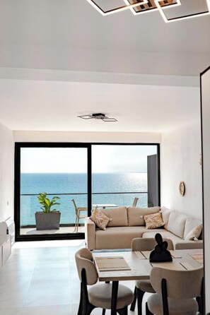 A modern living room with a large sliding glass door leading to a balcony with a view of the ocean.