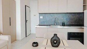 A modern kitchen with a sink, stove, and dishwasher, and a dining area with a vase and placemats. - SeaScape Residence (Borsh)
