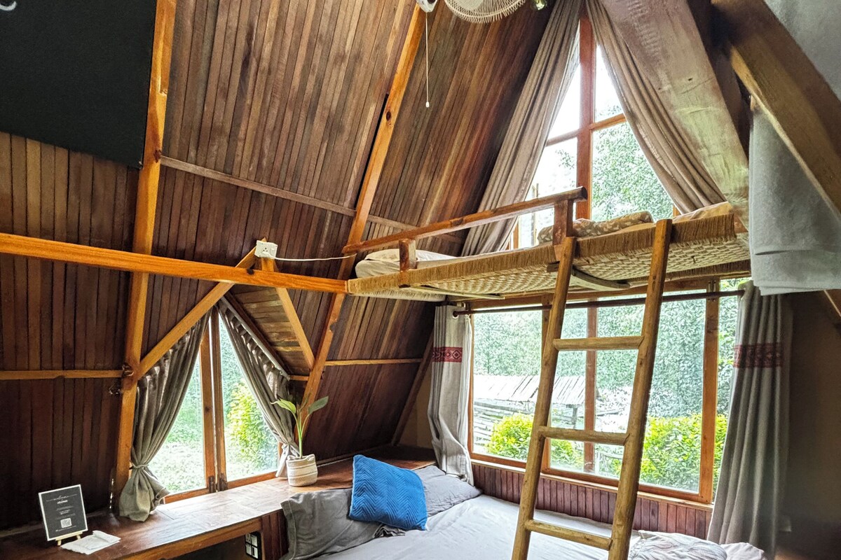 Una habitación rústica con cama de altillo, un escritorio pequeño y un ventilador.