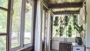 Ein Zimmer mit großen Fenstern, einer Korbsitzbank, einem Bett und Topfpflanzen.