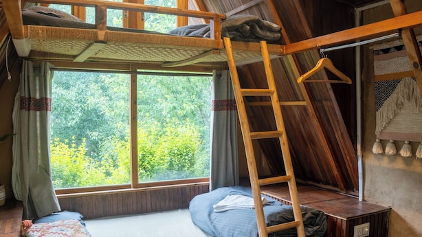 Ein Schlafzimmer im Loft-Stil mit einer Holzleiter, einem Etagenbett und einem großen Fenster mit Blick auf Grünflächen.