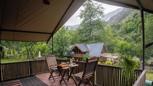 Ein überdachter Außenbereich mit Holztisch und -stühlen, einem Metall-Vordach und Blick auf einen bewaldeten Berg.