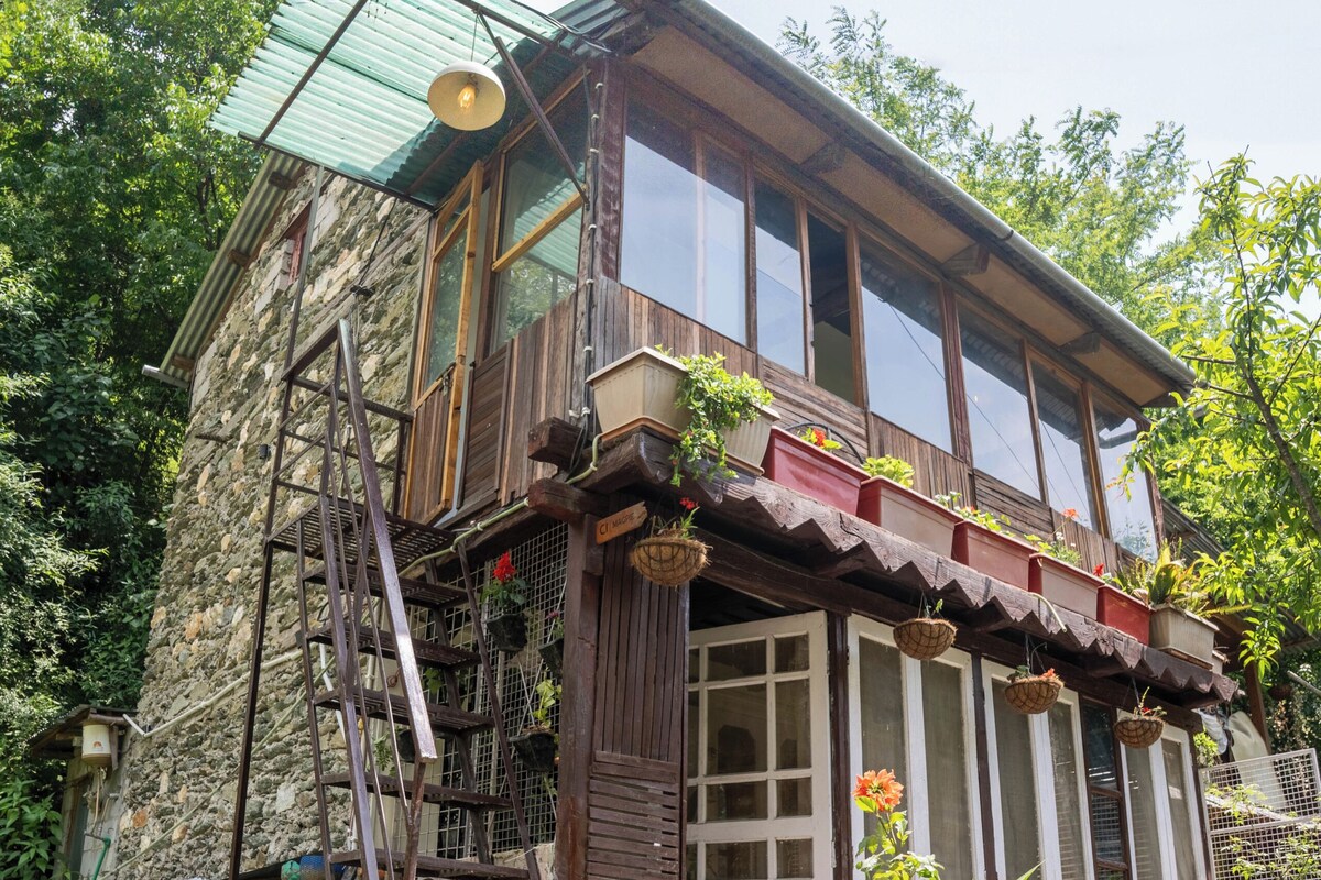 Un edificio rústico de piedra con un balcón de madera, una escalera y macetas colgantes.