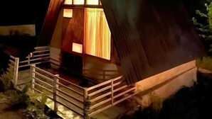Eine kleine Holzhütte mit einem Dreiecks-Dach, einem Balkon und einem beleuchteten Innenraum.