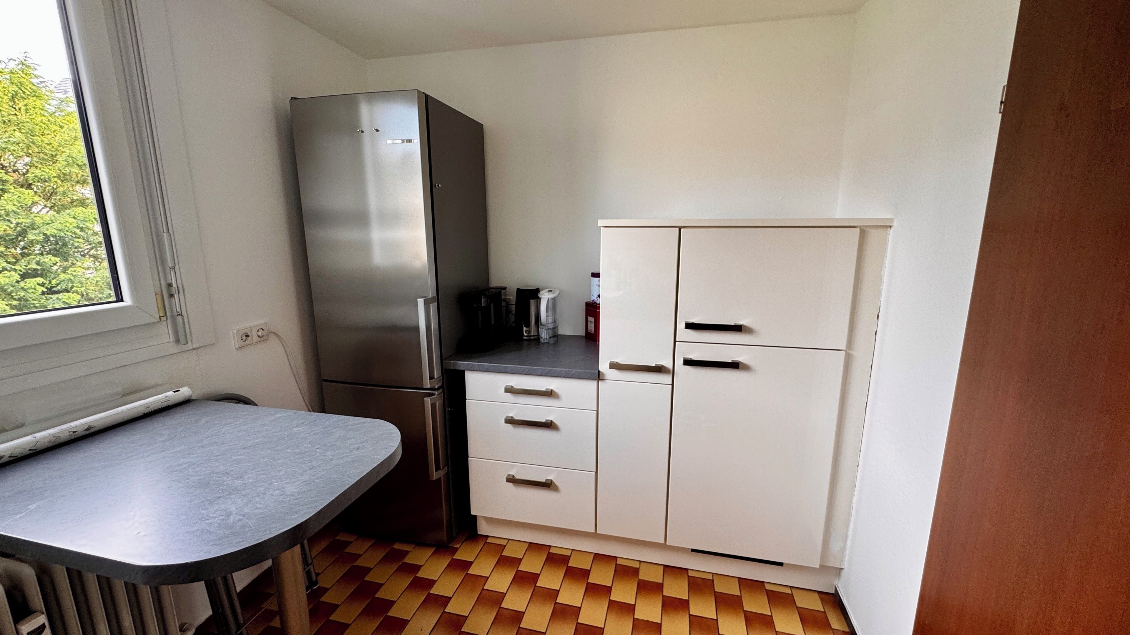 Una cocina compacta con refrigerador, una pequeña encimera y un ventanal.
