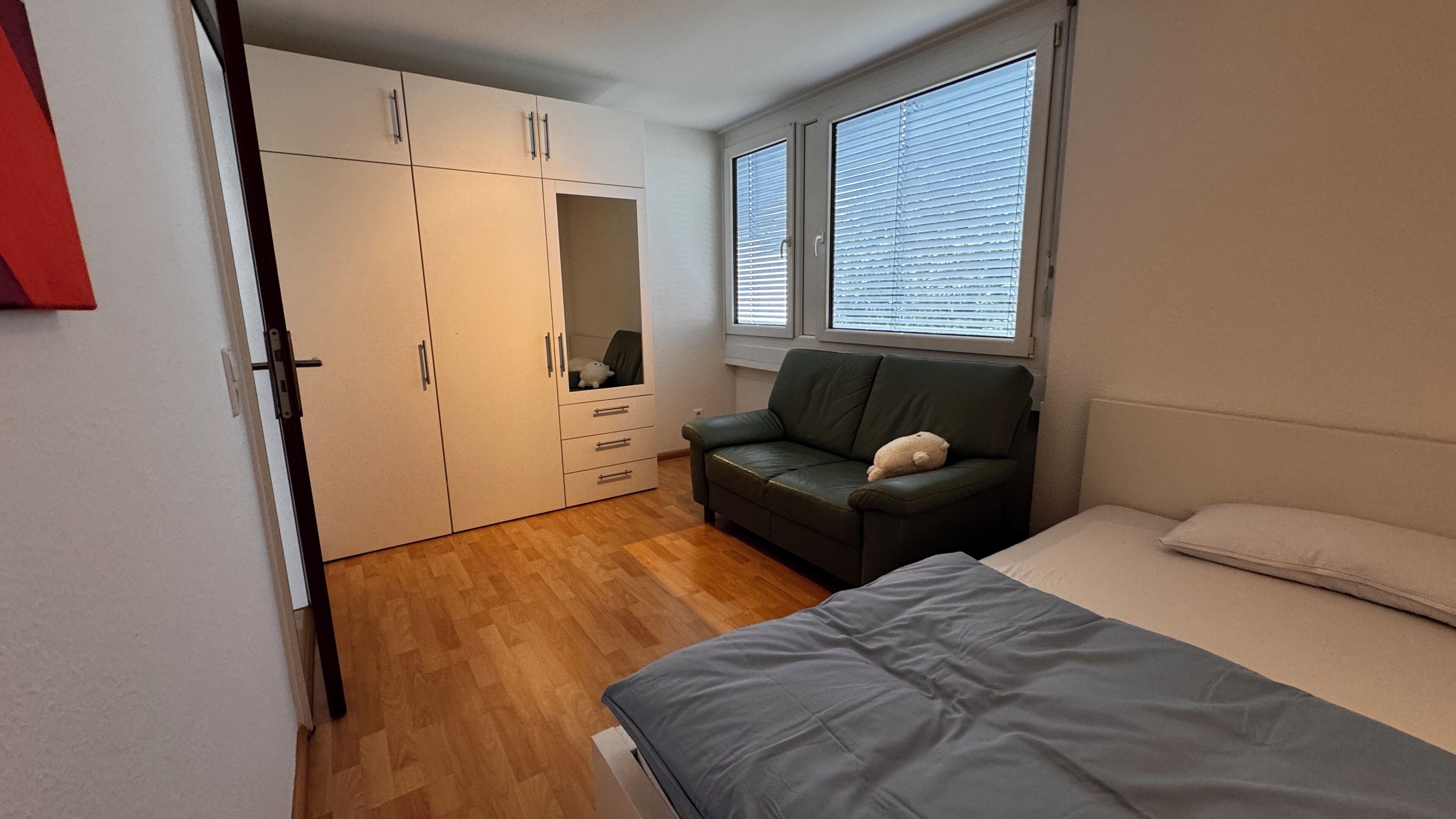 Un dormitorio con una cama, un sofá verde, un armario y una ventana con persianas.