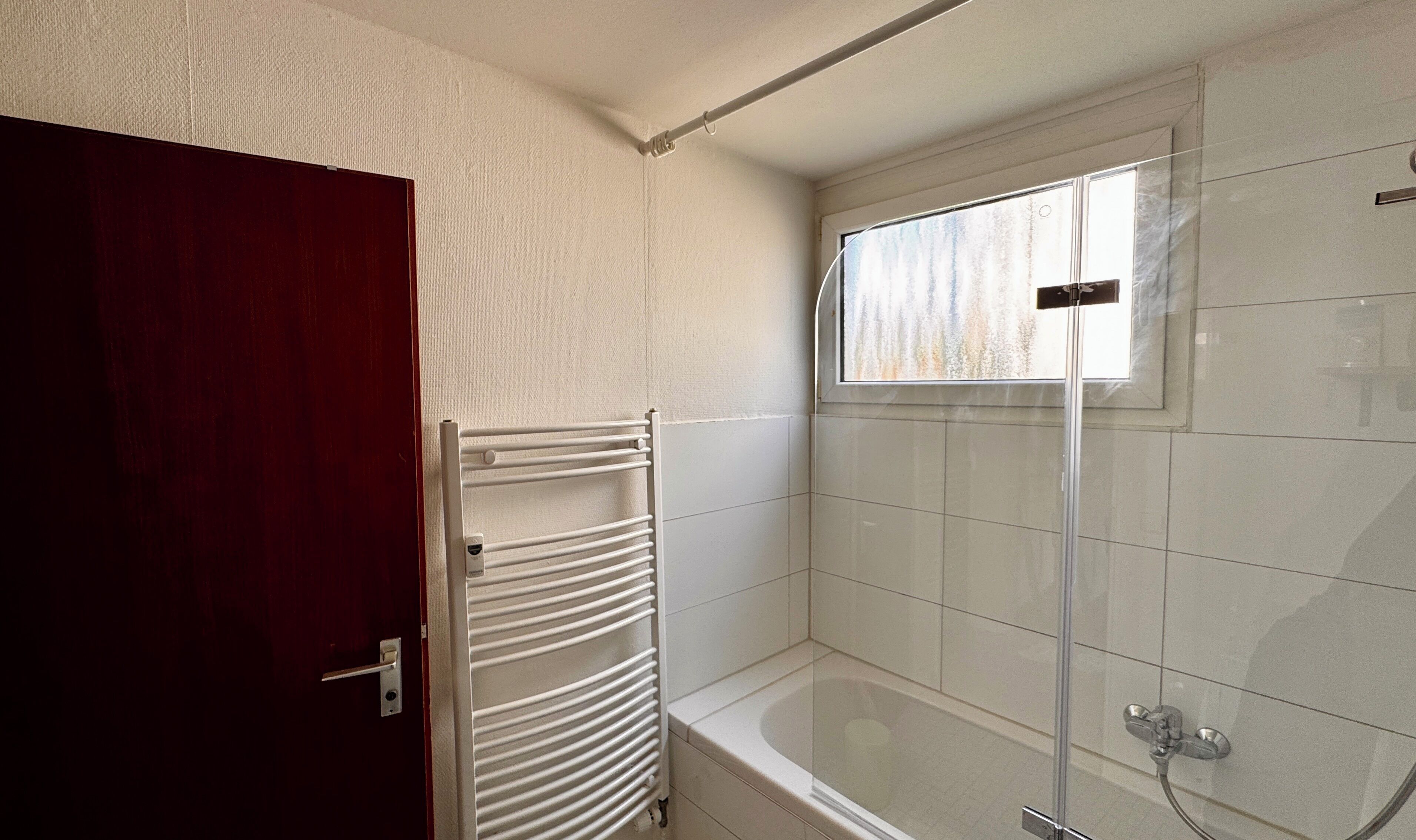 A bathroom with a bathtub, a window, and a towel rack.