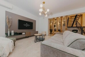 Ein modernes Wohnzimmer mit Flachbildfernseher, Sofa, Couchtisch und einer Treppe.