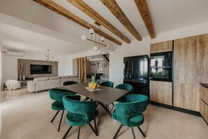 Ein moderner Essbereich mit Holzboden, einem zentralen Tisch mit Stühlen und einer Küche im Hintergrund.