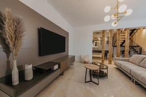 Ein modernes Wohnzimmer mit Flachbildfernseher, einer Couch, einem Couchtisch und einer Treppe, die zu einer oberen Ebene führt.
