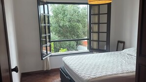 A bedroom with a bed, a window with a view of greenery, and a hanging lamp. - Charming 3-bedroom house in Cascais perfect for your getaway (Cascais)