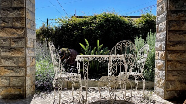 A stone wall with a metal table and chairs in a garden area. - Charming 3-bedroom house in Cascais perfect for your getaway (Cascais)
